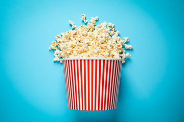 Overturned paper bucket with delicious popcorn on light blue background, top view
