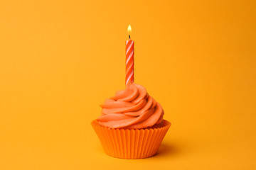 Delicious birthday cupcake with orange cream and burning candle on yellow background