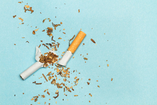 Cigarrillo roto partido por la mitad sobre fondo liso azul. Vista superior. Copy space. Concepto:Salud