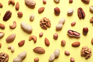Different delicious nuts on yellow background, flat lay