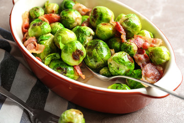 Delicious Brussels sprouts with bacon in baking dish on marble table, closeup