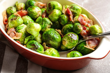 Delicious Brussels sprouts with bacon in baking dish on table, closeup