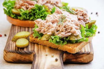 Homemade tuna salad sandwiches on cutting board with pickles aside