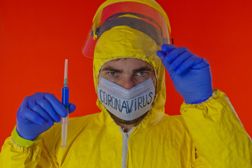 Man in yellow chemical protection suit and face protective mask coronavirus. Without glasses. Protective helmet. Hands in blue gloves. Blue vaccine syringe.