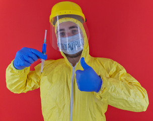 Man in yellow chemical protection suit and face protective mask "coronavirus". Without glasses. Protective helmet. Hands in blue gloves. Blue vaccine syringe. Thumb up..