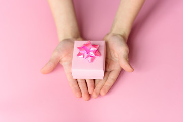 Hands with pink gift box with beautiful rose bow on pink background. St. Valentines day concept. Gift concept.