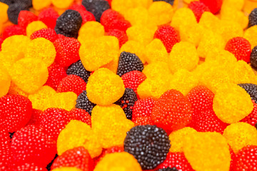 Bright yellow, black and red marmalade chewing sweets in the shape of berries. Sweet beautiful delicacy made from gel fruit juices. Colorful background. Randomly heaped goodies.