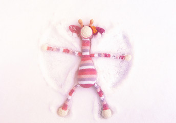  A toy striped pink giraffe lies on the snow, rejoices and waves its paws.