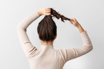 Young woman doing her hair on light background