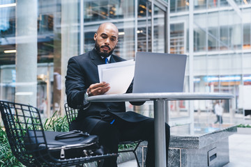 Elegant businessman checking documents while using laptop