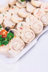 Ham and cheese pinwheels with seasoned cream spread slices on plate with vegetable decoration.