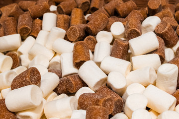 Many cylindrical chewing sweets in sugar sprinkles of white and brown. Tasty aromatic delicacy in the store counter.