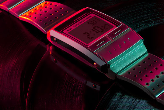 Vintage digital watch lies on multiple vinyl records, blue and red purple light, disco colors, idyllic background, wrist watch. Casio