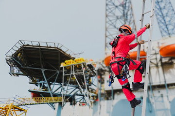 Worker wearing seat belts safety full harness go up the stairs fixed ladder on rig driling and heliport parking lot background during maintenance in shipyard.