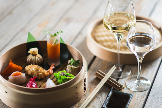Several different traditional Chinese dimsum dumplings in a wooden basket cooked for guests on a wooden table in a restaurant.