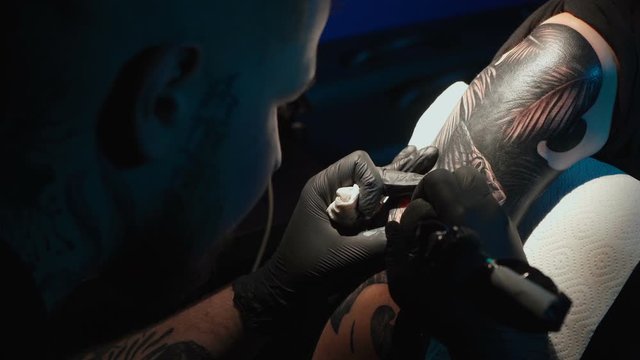 Close up video of man doing black tattoo of snake for woman in studio