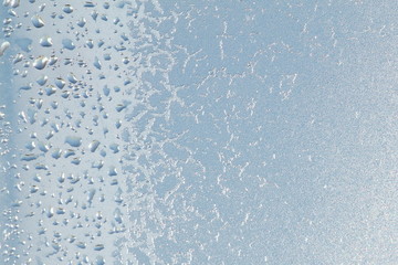 Blue window glass covered hoarfrost ice pattern texture with water drops. Cold nature winter background