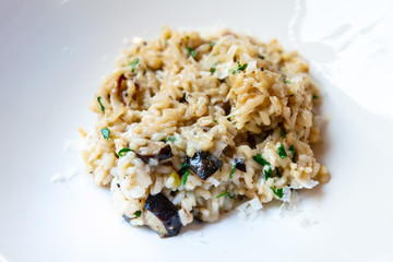 Delicious Italian vegetarian risotto cooked with mushrooms and onions served in white plate.
