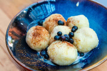 Six homemade sweet dumplings served with vanilla cream and blueberries in blue ceramic vintage bowl