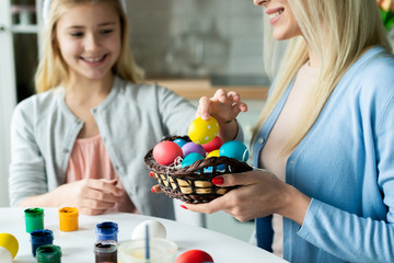 Happy family preparing for Easter. Daughter takes a colorful egg and her mother  holding a basket.