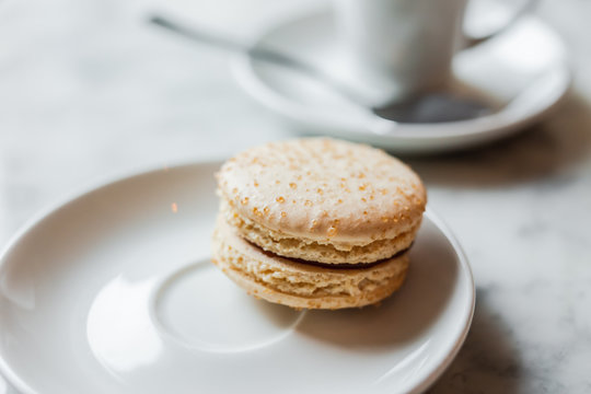A close up photo of a macaron with salted caramel on a white saucer, a cup of coffee in the background