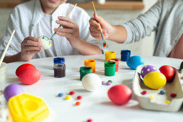 Сhildren's hands hold brushes and painting an Easter eggs. Colorful paints and eggs lie on the table.- Cropping image