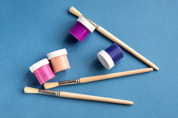 Colorful vibrant cans of gouache paint and brushes isolated on color blue background. Colorful...