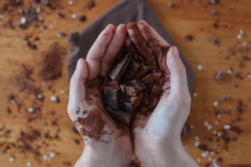 Hands of young caucasian woman catching ounces of healthy chocolate with pure cocoa powder