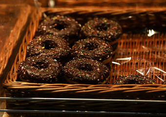 Donut de chocolate con pepitas de colores en una bandeja de madera.