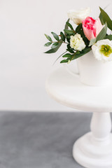 Spring bouquet in white vase on wooden white stand. Roses, tulips and lisianthus.
