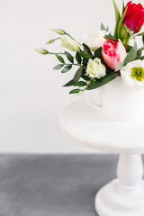 Spring bouquet in white vase on wooden white stand. Roses, tulips and lisianthus.