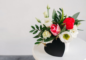 Black board heart copyspace. Spring bouquet in white vase on wooden white stand. Roses, tulips and lisianthus.