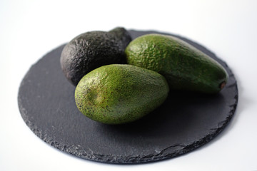 Three green avocados on a black board on a white background. Raw whole avocados on the board. Green avocado and with a darker skin.