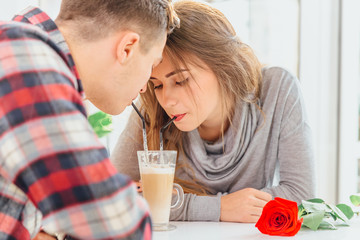 Cropped shot of romantic couple enjoying each others company, drinking coffee from the same glass with straws, sitting in cafe.