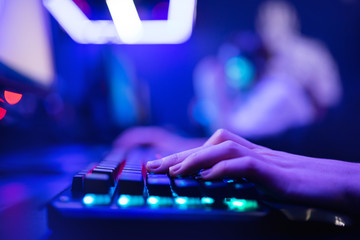 Professional online gamer hand fingers mechanical keyboard in neon color blur background. Soft...