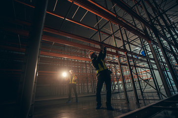 Two technician repairing machine shelf in dark room warehouse.