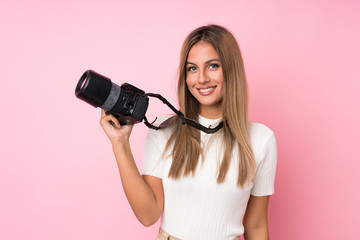 Young blonde woman over isolated pink background with a professional camera