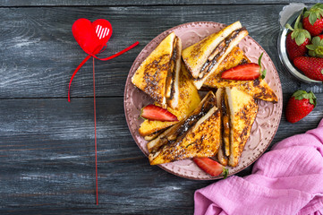 Sweet french toasts with banana, chocolate, strawberries on a wooden background. Tasty breakfast. Top view