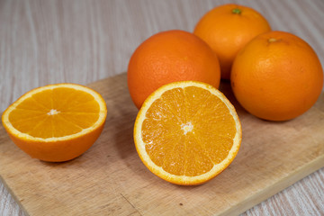 Selective focus on a sliced organic orange on a chopping board next to three oranges.