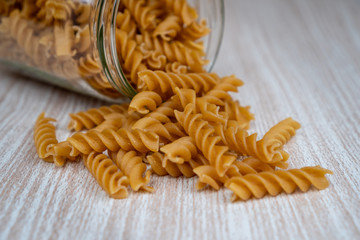 Dry Italian wholegrain wheat pasta spilling from a glass jar. Healthy nutrient rich alternatives. Wholefood plant based diet.