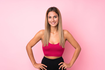 Young sport blonde woman over isolated pink background posing with arms at hip and smiling