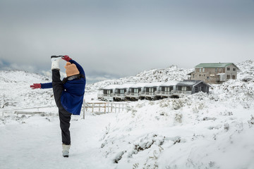 Female doing a standing yoga splits pose in the snow, with Ben Lomond ski resort background, Tasmania, Australia