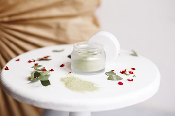 Fototapeta na wymiar Powder cosmetic mask. Glass jar with matcha on a white background with dry petals.