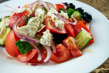 Classic Greek salad with tomatoes, onions, cucumber, feta cheese and black olives in white plate on a light background. Close up view. Food flat lay