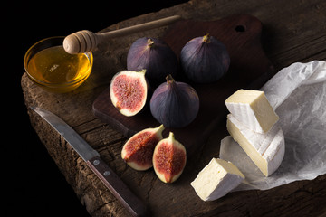 Fresh ripe figs. Breakfast with figs, cheese, honey and nuts. A few figs on an old wooden background. Whole figs and one fig sliced. Fresh fruits, purple figs on the wooden background. Autumn harvest.