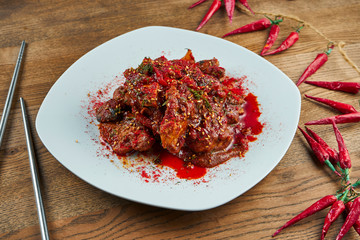 Appetizing, spicy meat cooked according to a traditional Korean recipe with hot pepper, tomatoes on a white plate on a wooden background. Tasty stew meat