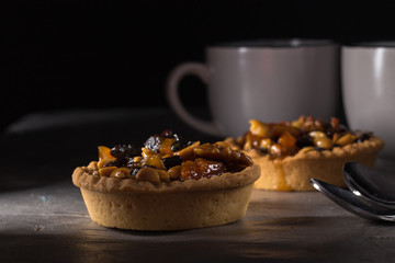 tart with salted caramel. Tart with nuts and caramel on a rustic background. Tartlets with dried fruits and nuts. Homemade tartlets with fruit and coffee. Dessert on a gray concrete table. Free space 