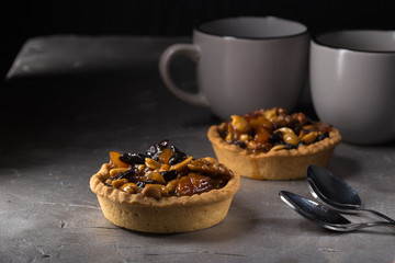 tart with salted caramel. Tart with nuts and caramel on a rustic background. Tartlets with dried fruits and nuts. Homemade tartlets with fruit and coffee. Dessert on a gray concrete table. Free space 