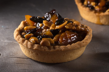 tart with salted caramel. Tart with nuts and caramel on a rustic background. Tartlets with dried fruits and nuts. Homemade tartlets with fruit and coffee. Dessert on a gray concrete table. Free space 