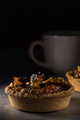 tart with salted caramel. Tart with nuts and caramel on a rustic background. Tartlets with dried fruits and nuts. Homemade tartlets with fruit and coffee. Dessert on a gray concrete table. Free space 